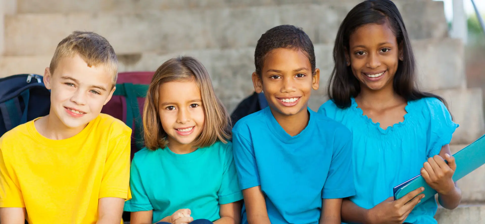 Four children with backbacks and holding folders
