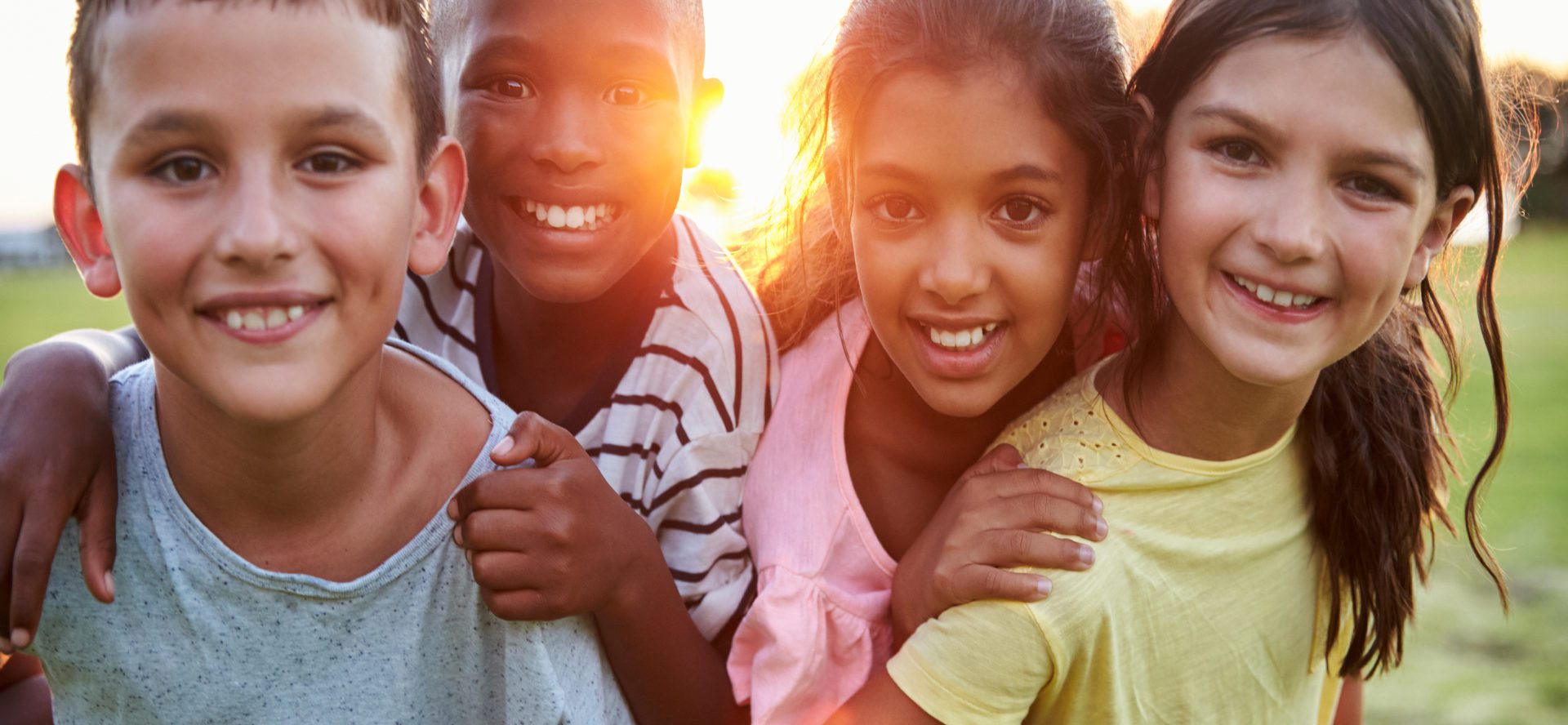 Four children smiling with sunset behind them